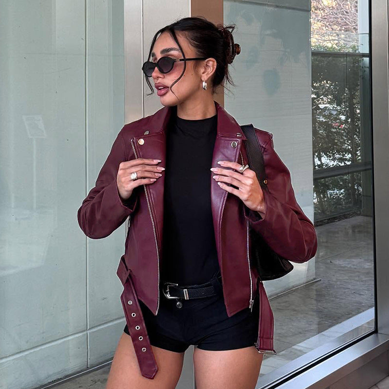 Women's fitted biker jacket made of faux leather with asymmetrical zipper, metallic details, and waist belt Mune Fashion