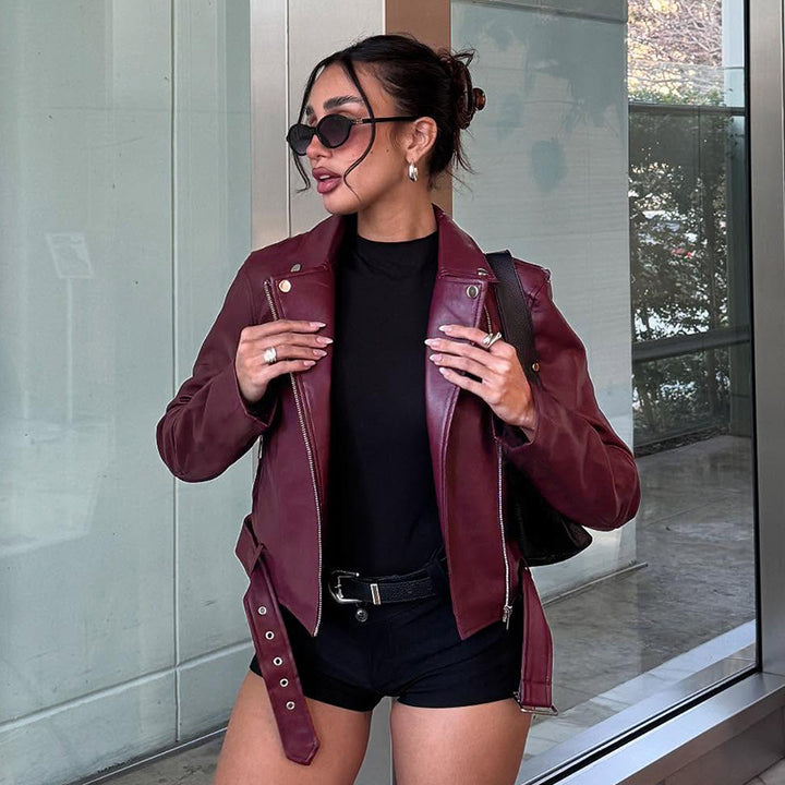 Women's fitted biker jacket made of faux leather with asymmetrical zipper, metallic details, and waist belt Mune Fashion